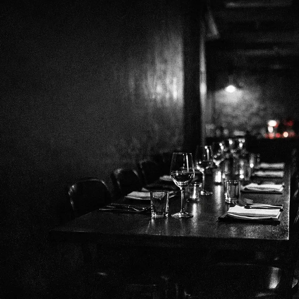 A shadowed dining table in Chance and Hearth’s ember-lit interior